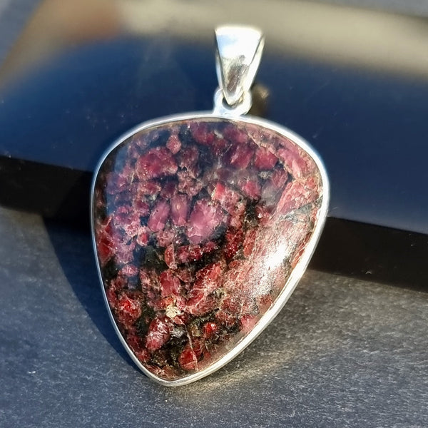 Natural Eudialyte gemstone displaying rich raspberry-red colouring with contrasting black and white mineral patterns in a polished finish.